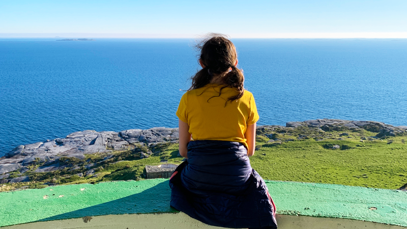 Jente sitter på Fjøløy i en kanonstilling og ser utover havet.