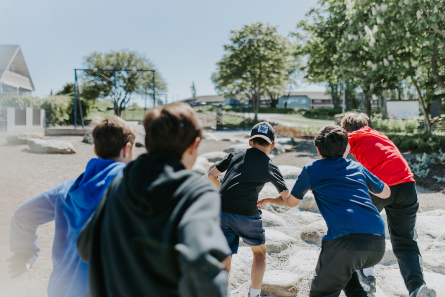 Fem gutter sett bakfra, de springer på en lekeplass/friområde