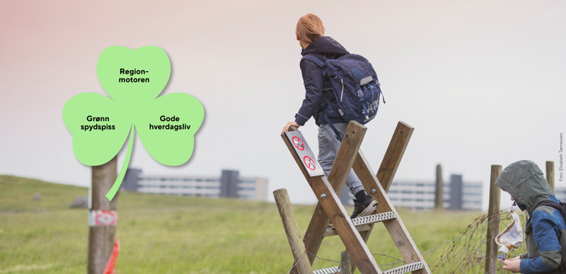 Gutt som klatrer over gjerdeklyvar og speider ut over landskapet. Ullandhaug-blokkene (Jernalderveien) i bakgrunnen. Foto: Elisabeth Tønnessen