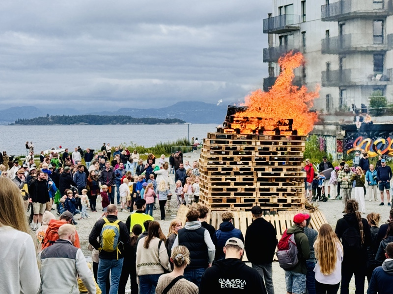 sankthansbål med mange folk som ser på. Deler av Tou scene til høyre i bildet.
