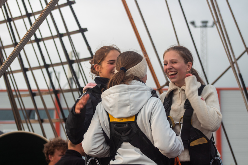 tre jenter smilende om bord i en seilskute.
