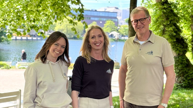 To damer og en mann som står i en park og smiler.