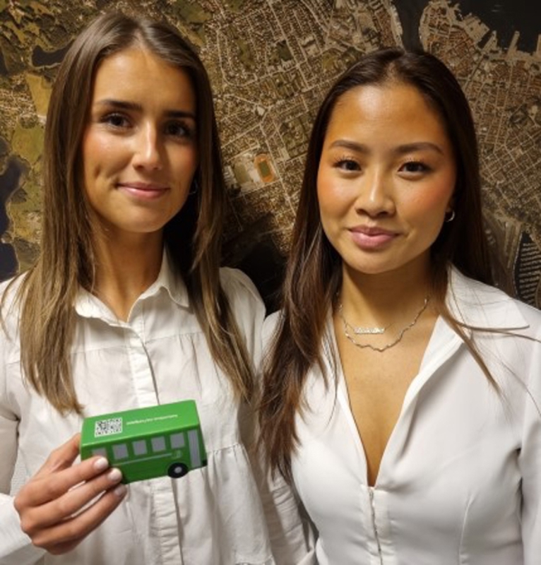 To unge kvinner holder en liten modell av en grønn buss.