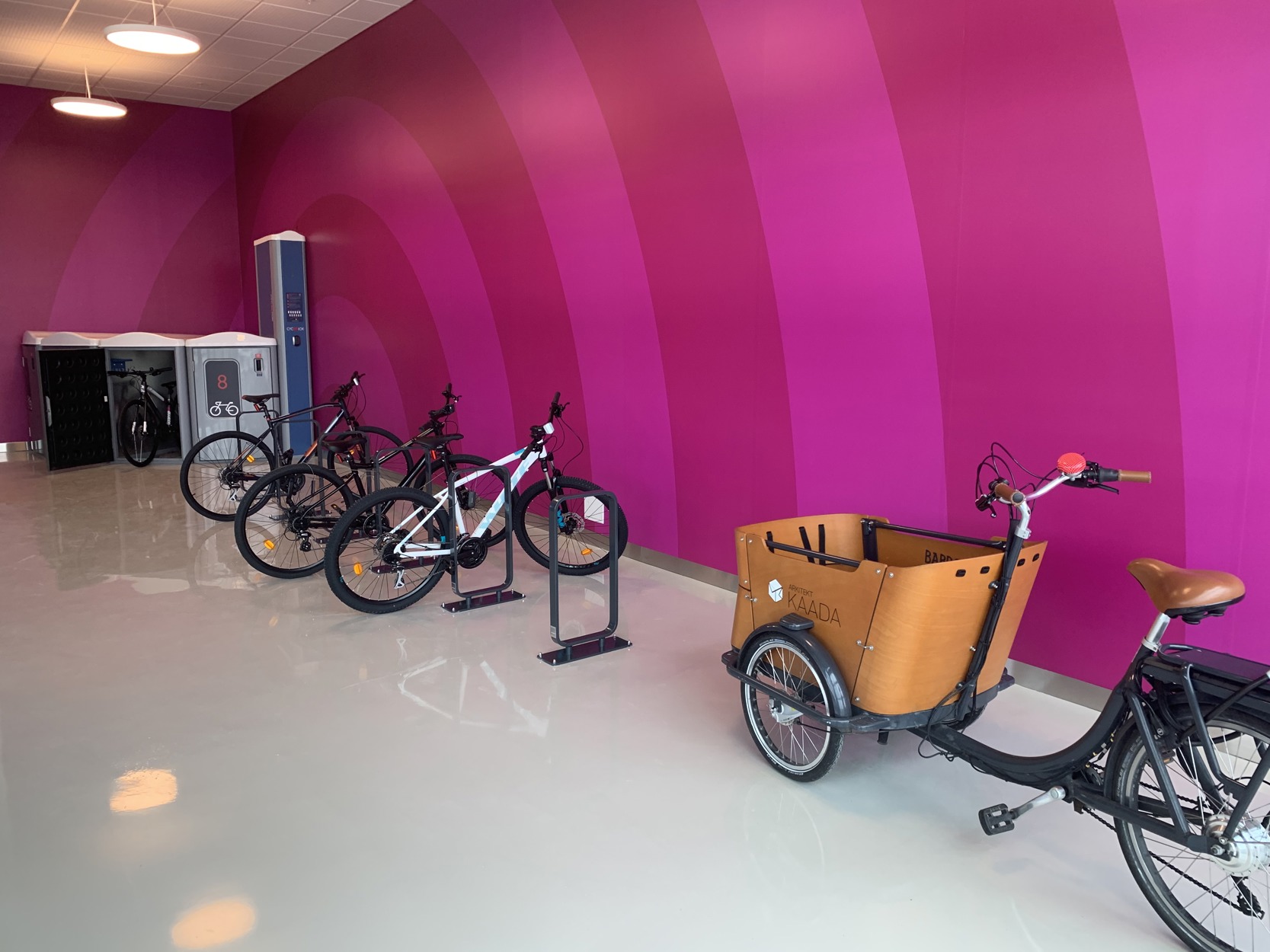 Bilder viser et innendørs sykkelparkeringsanlegg med sykkelbokser, stativer og oppstillingsplass til sykkelvogn