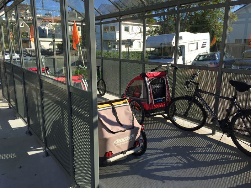 I et sykkelvognhus med store vinduer står fire sykkelvogn og en sykkel parkert.